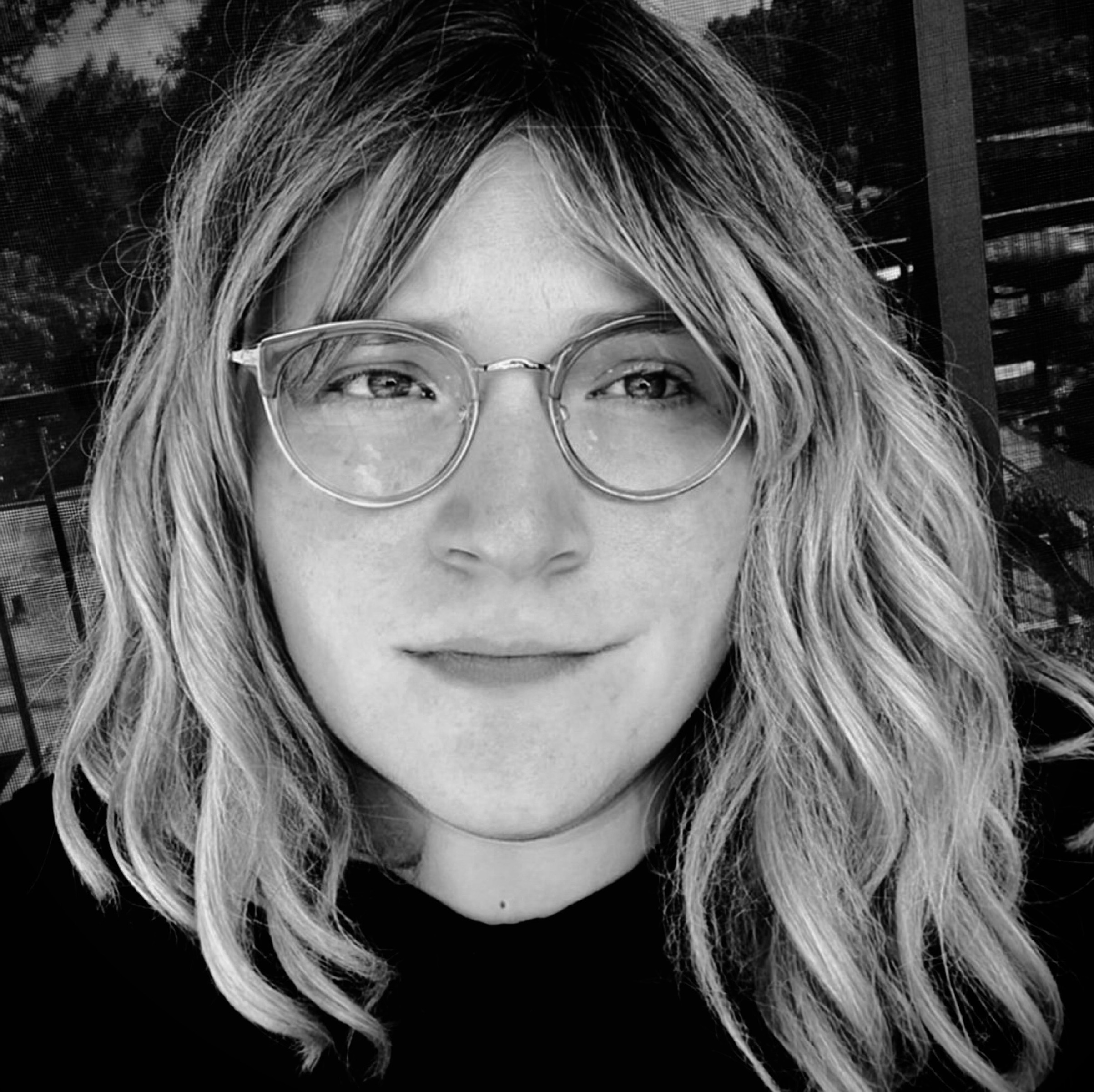 A grayscale photograph of me. I have white skin, silvery hair, and a pair of glasses framing a set of wide eyes. I'm smiling and looking off to the right.